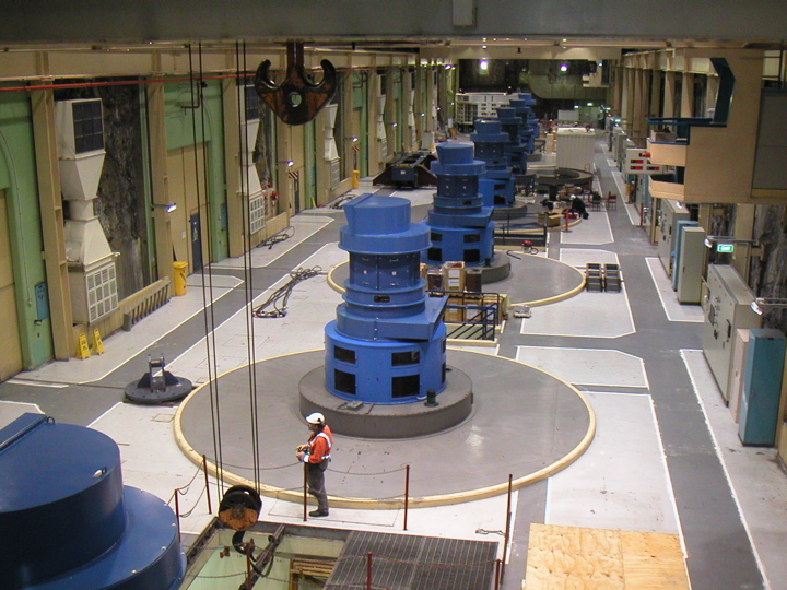 The project is literally "groundbreaking" because it relies on holes drilled deep into the schist bedrock of Fiordland.  Instead of water falling over a dam, the water falls straight down 8 drilled tubes at the edge of Lake Manapouri to reach the turbines, which spin the generators seen here in the massive underground equipment room.  A truck access tunnel spirals down through the mountain to get here, almost as low as sea level.  Nearly-horizontal tunnels take the water from the turbines out to Doubtful sound, about 20 km away.  The project took nearly 15 years to complete.